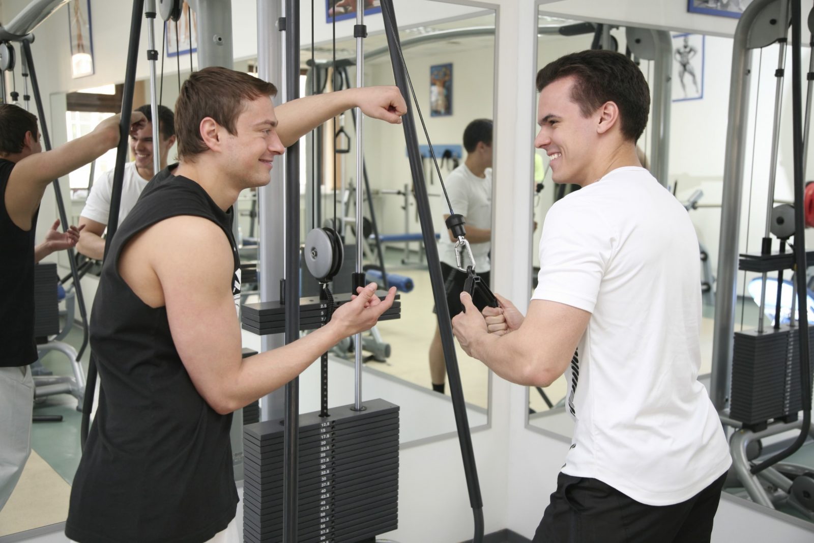 Два парня смеются, беседуют во время выполнения упражнения в тренажерном зале