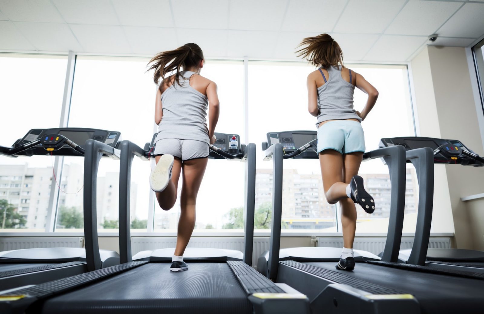 Две девушки в спортзале выполняют пробежку на беговой дорожке