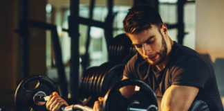 Новичок в тренажерном зале выполняет подъем штанги на бицепс в скамье Скота