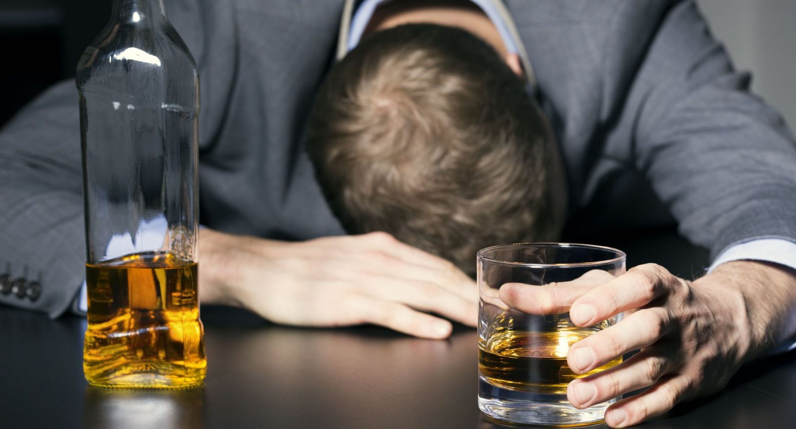 Мужчина со стаканом алкоголя сидит поникшим за столом