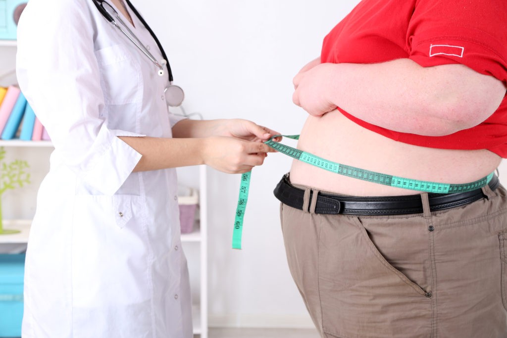 Девушка в белом халате измеряет объем живота у толстого мужчины