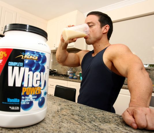 Накаченный атлет пьет из шейкера пьет сывороточный протеин
