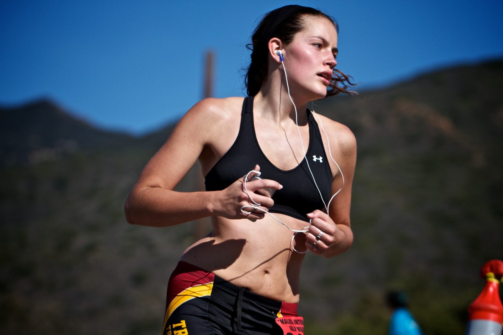 Девушка-спортсменка в наушниках участвует в забеге