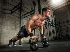 Атлет в шортах и голым торсом отжимается от гирь на полу