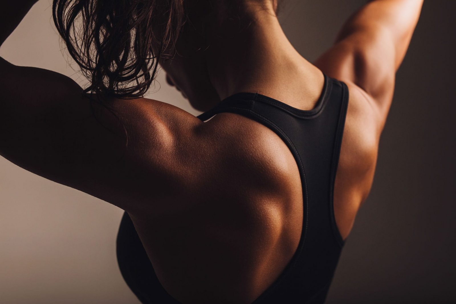 Девушка в черном топе демонстрирует крепкие мышцы спины