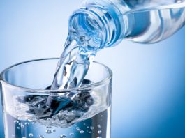 Чистую воду наливают в прозрачный стакан на голубом фоне