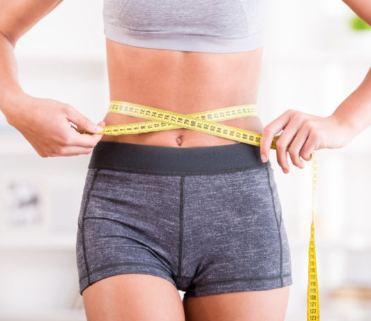 Спортивная девушка измеряет талию дома