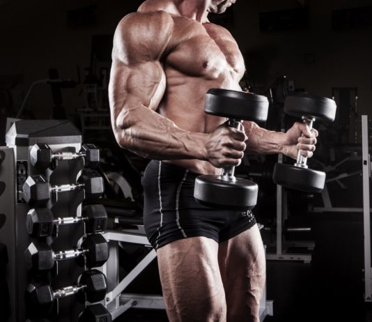 Мускулистый атлет в тренажерном зале с гантелями