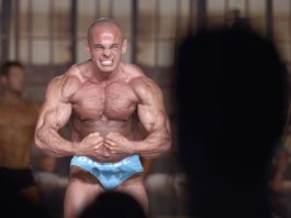 Накаченный бодибилдер на сцене позирует