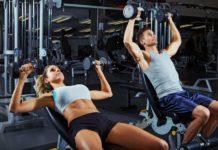 Парень и девушка в тренажерном зале выполняют силовые упражнения на плечи