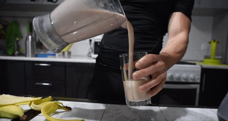 Культурист наливает из блендера в стакан протеиновый (белковый) коктейль