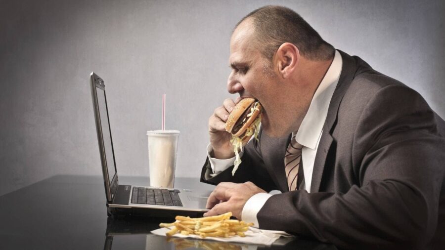 Нездоровый образ жизни: мужчина за ноутбуков кушает фастфуд